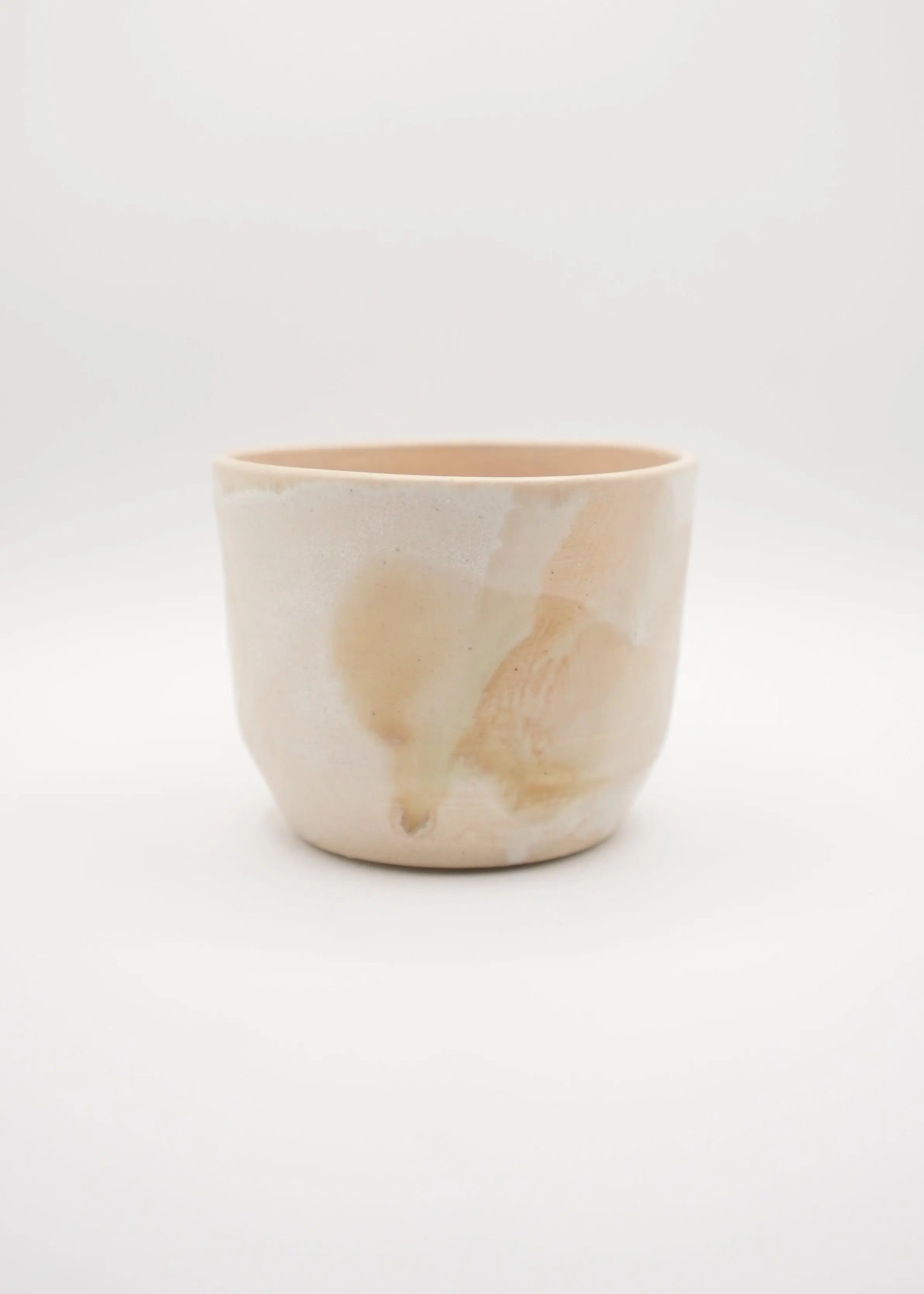 A small handmade ceramic cup with a textured, organic marbled pattern in soft beige, cream, and light brown tones, set against a seamless white background.
