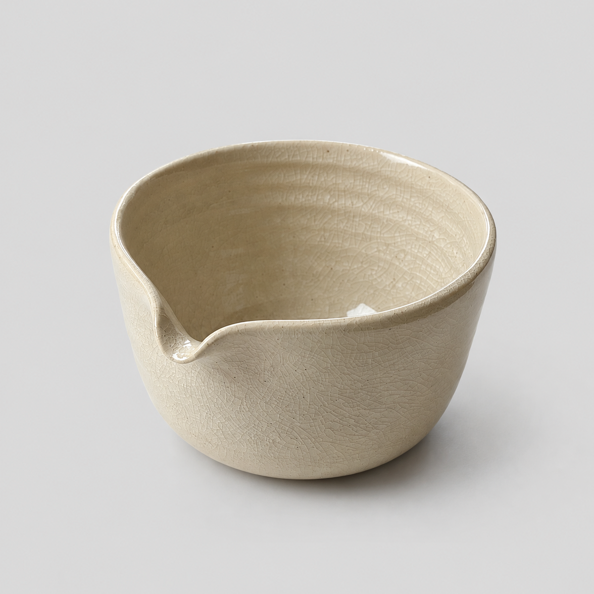 A handmade ceramic matcha bowl with a small pouring spout, featuring a textured, ribbed interior and a matte, earthy beige finish, set against a solid light gray background.