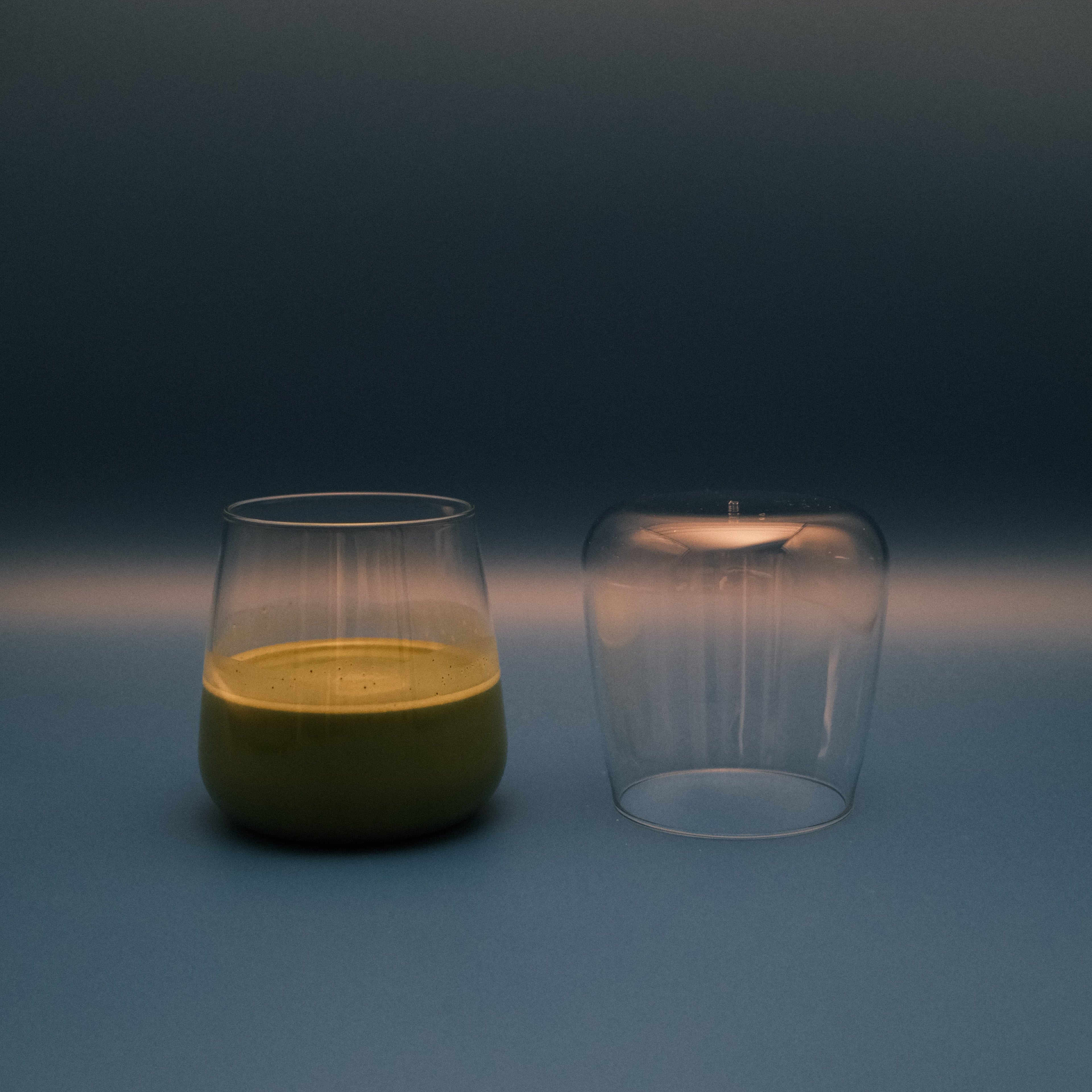 Two glass containers, one filled with matcha, on a gradient blue and gray background.