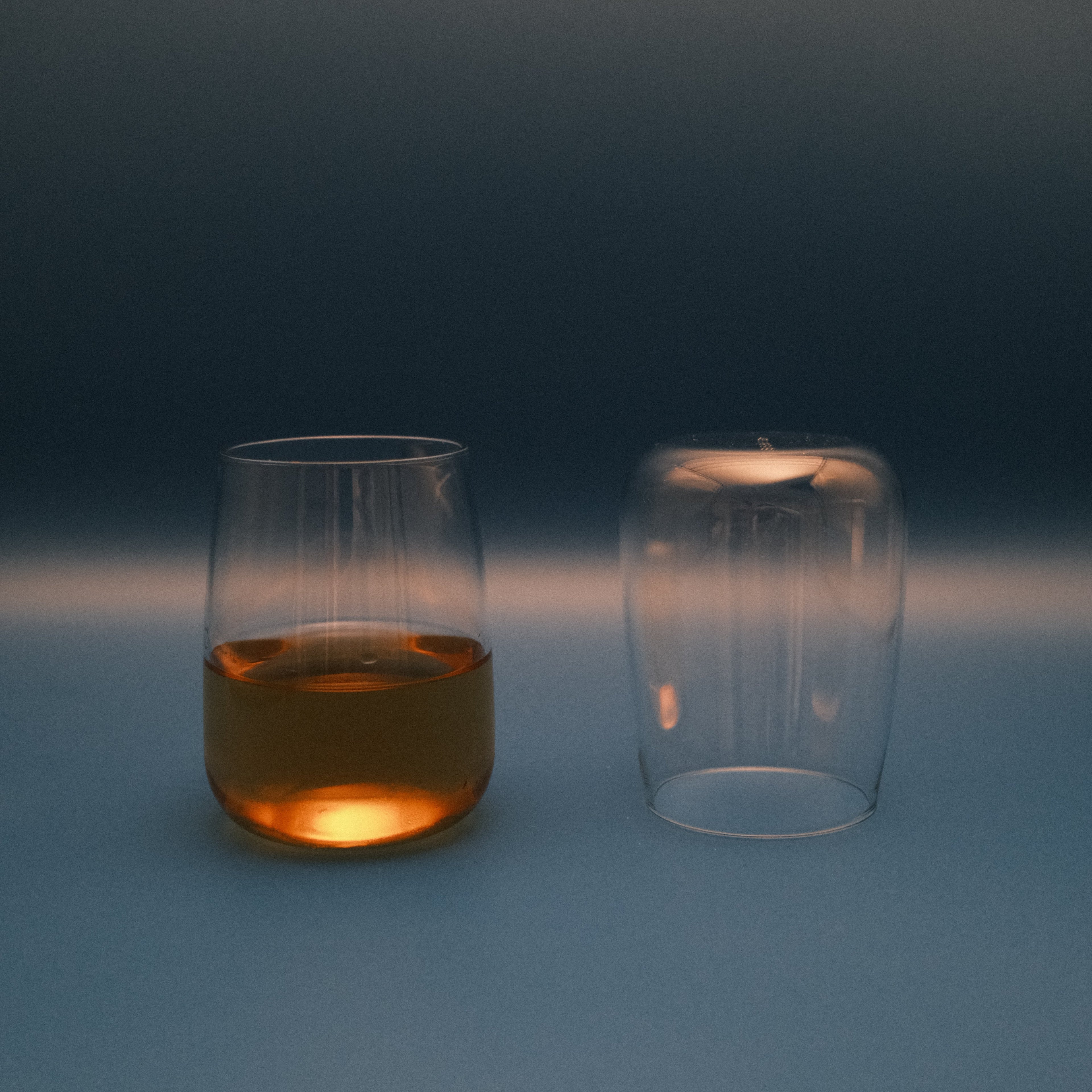 Two glass containers with one filled with a liquid on a gradient blue background