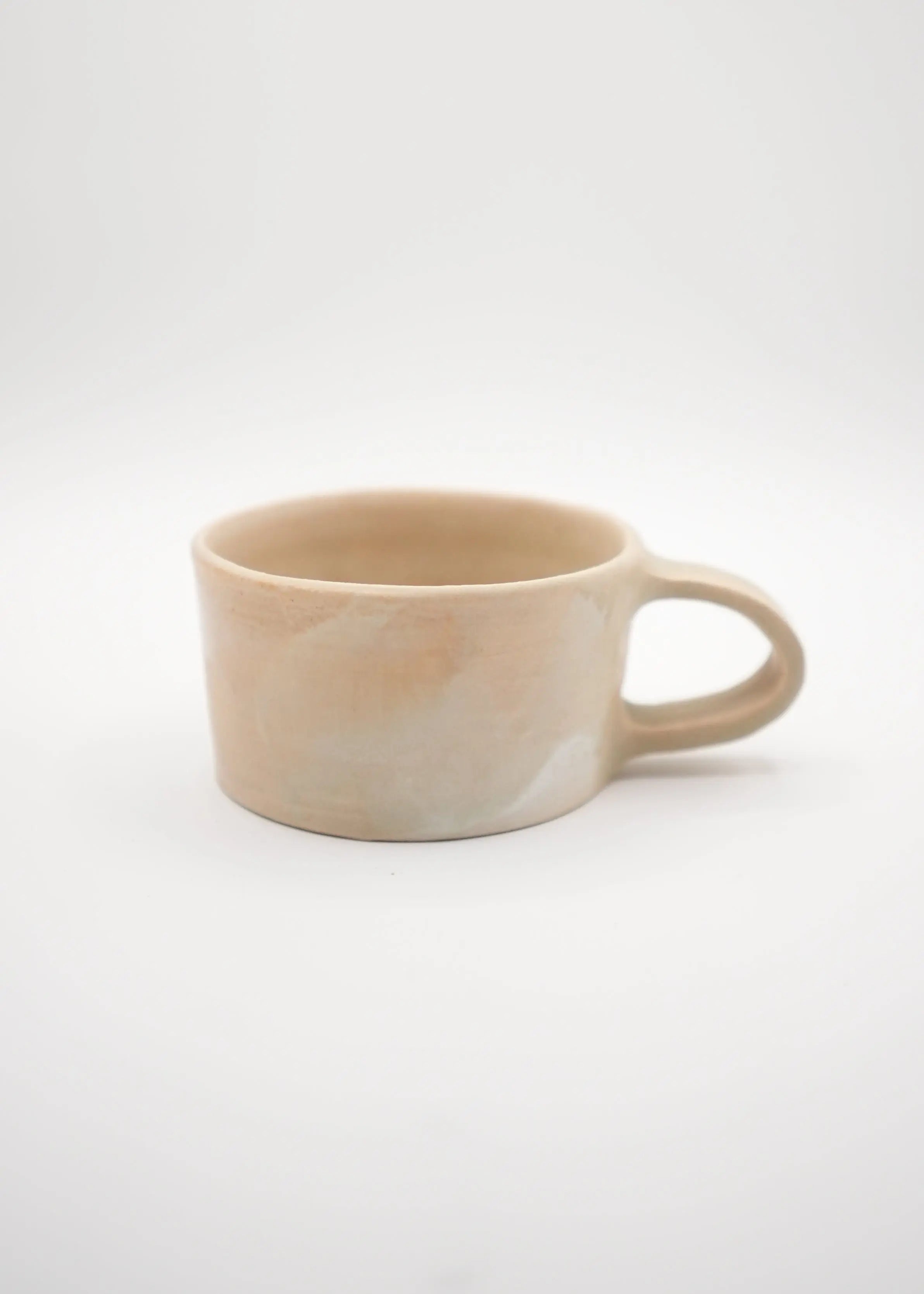 A minimalist handmade ceramic mug with a rounded body and a loop handle, featuring a soft beige and cream marbled glaze, set against a plain white studio background.
