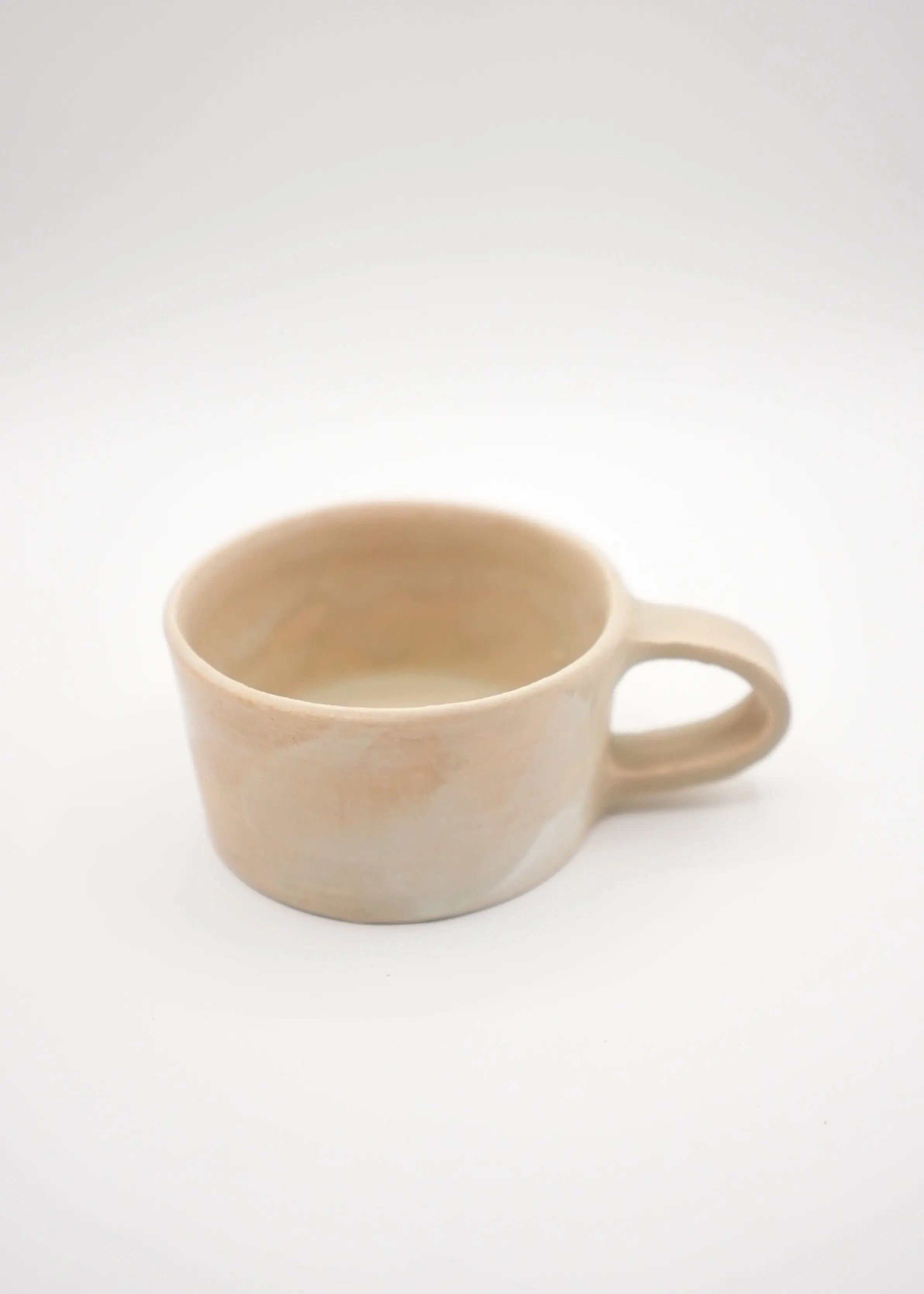A minimalist handmade ceramic cup with a handle, featuring a marbled beige and cream glaze, photographed on a seamless light gray background.
