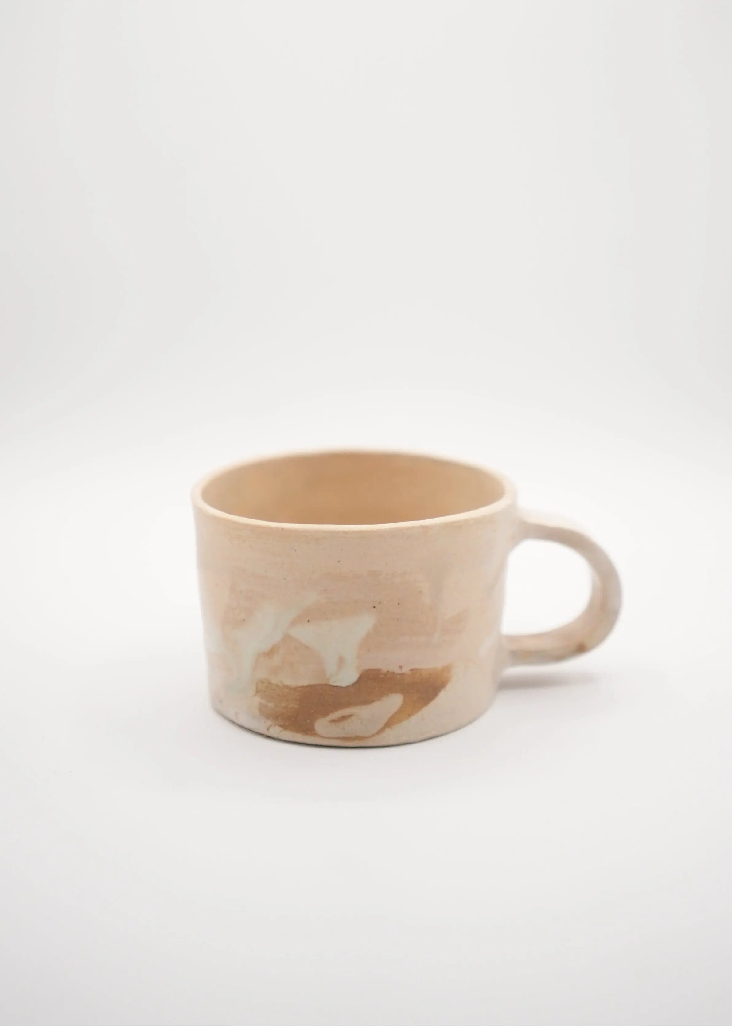 A handmade ceramic mug with a warm beige and brown marbled pattern, photographed against a seamless white background.