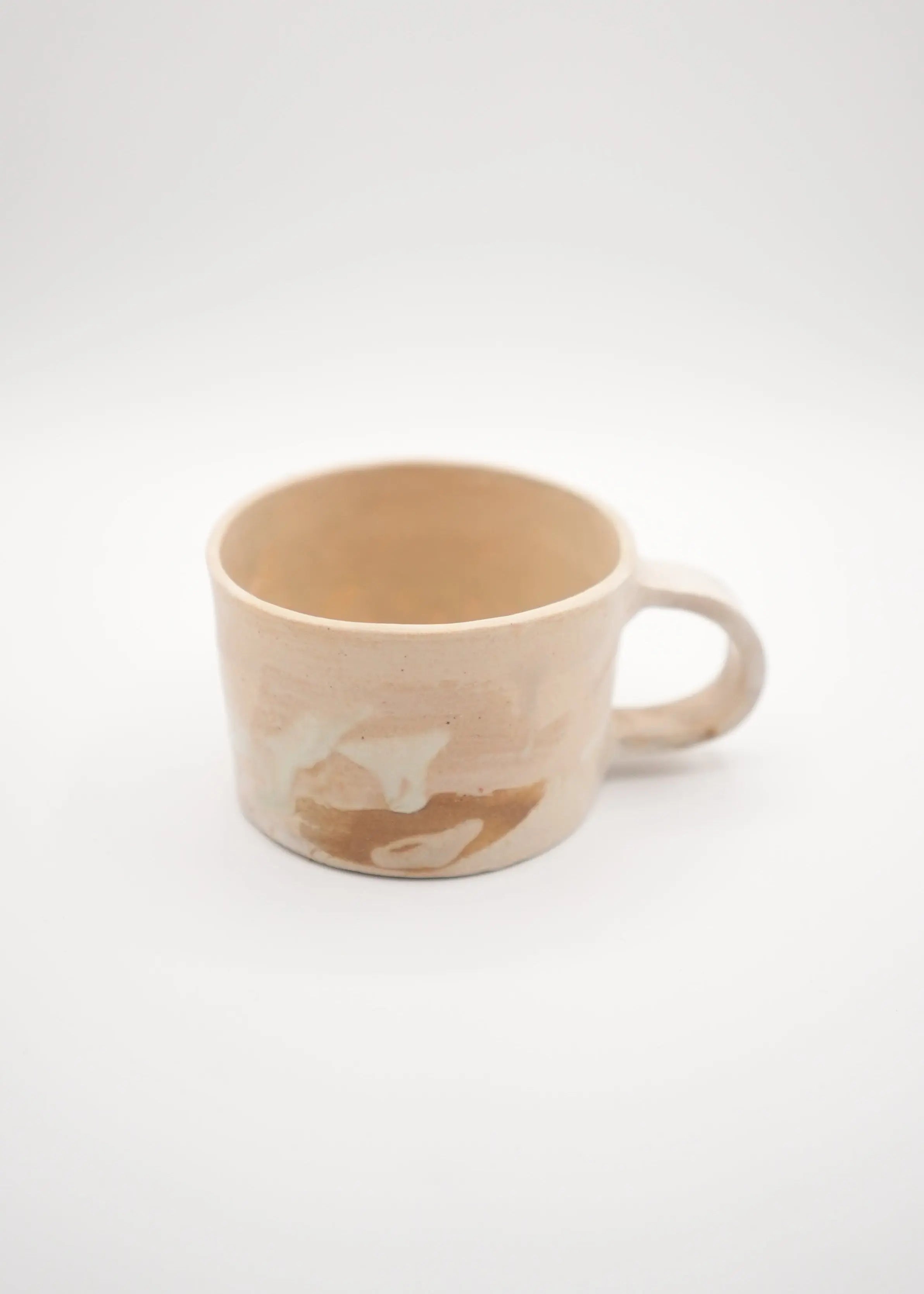 A handmade ceramic mug with a warm beige and brown marbled pattern, photographed on a seamless light gray background.