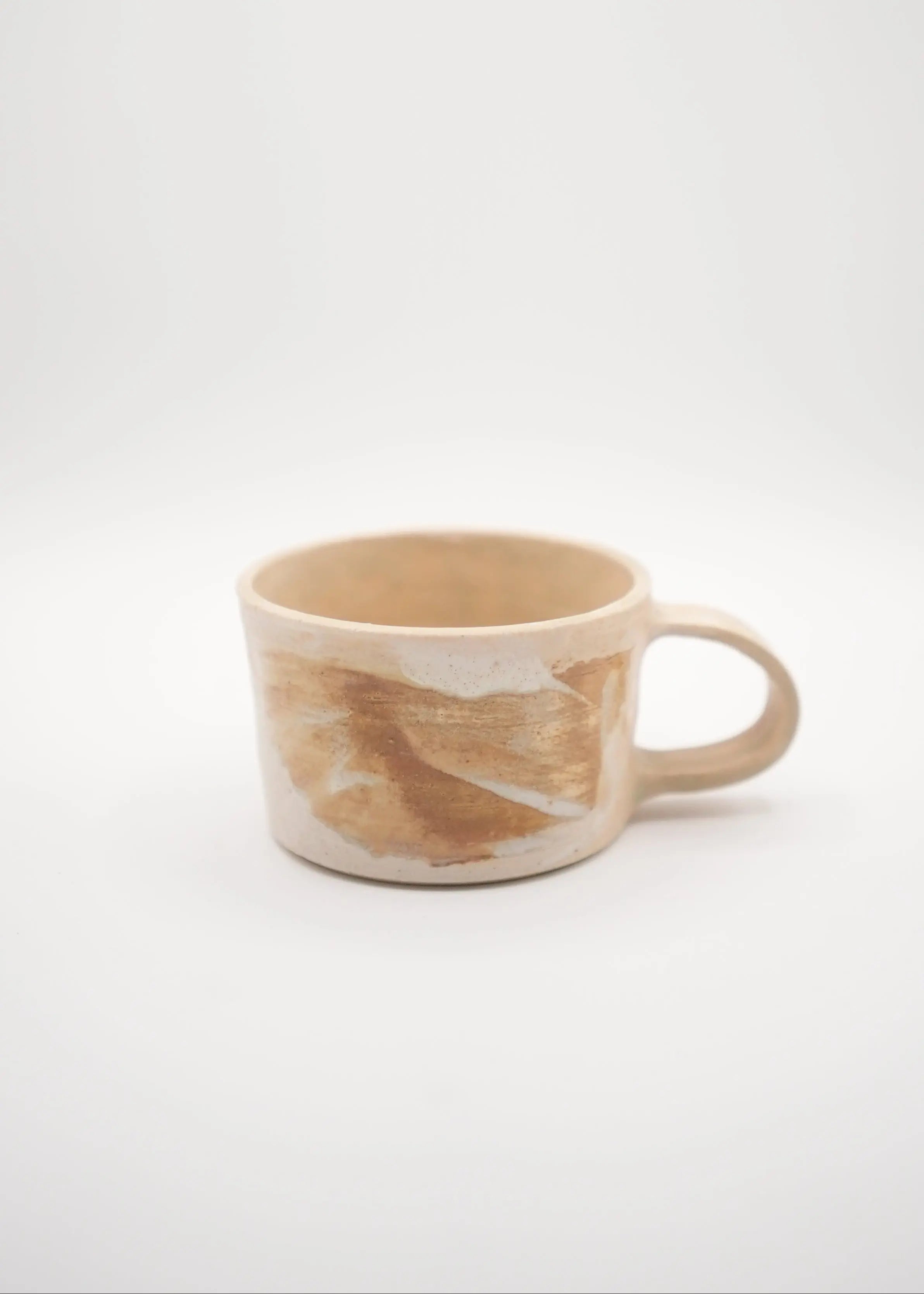 A handmade ceramic mug with a handle, featuring a textured, hand-painted design in warm beige, brown, and cream tones, set against a plain light gray background.