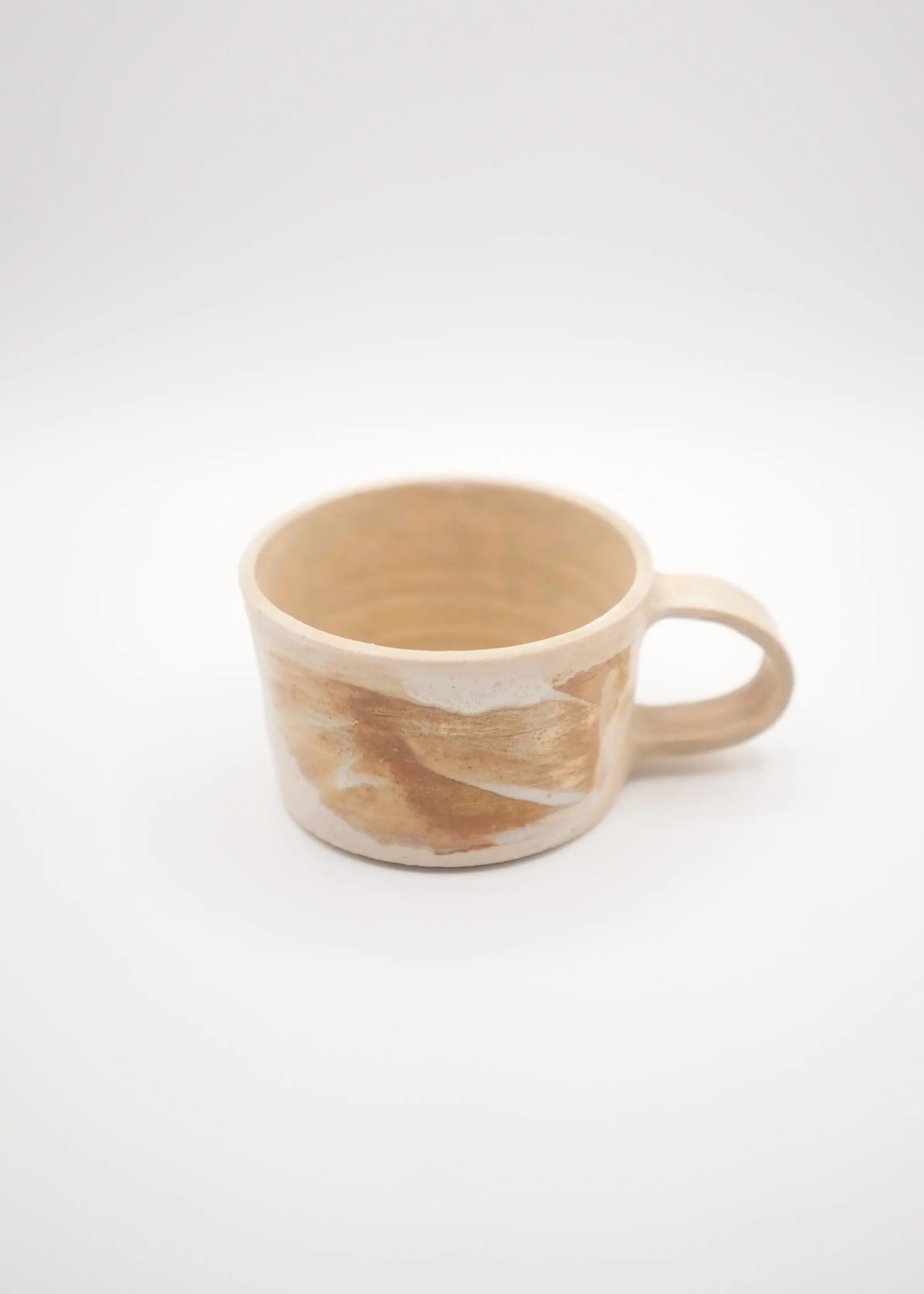 A handmade ceramic mug with a handle, featuring a marbled pattern of beige, cream, and light brown glaze, set against a plain white background.