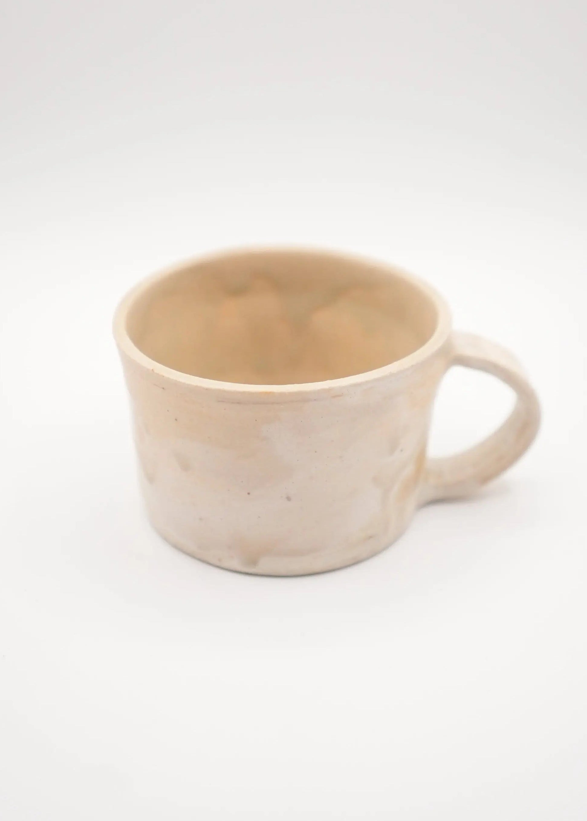 A handmade ceramic mug with a small handle, featuring a textured, speckled finish in a light cream-beige color, set against a plain white background.