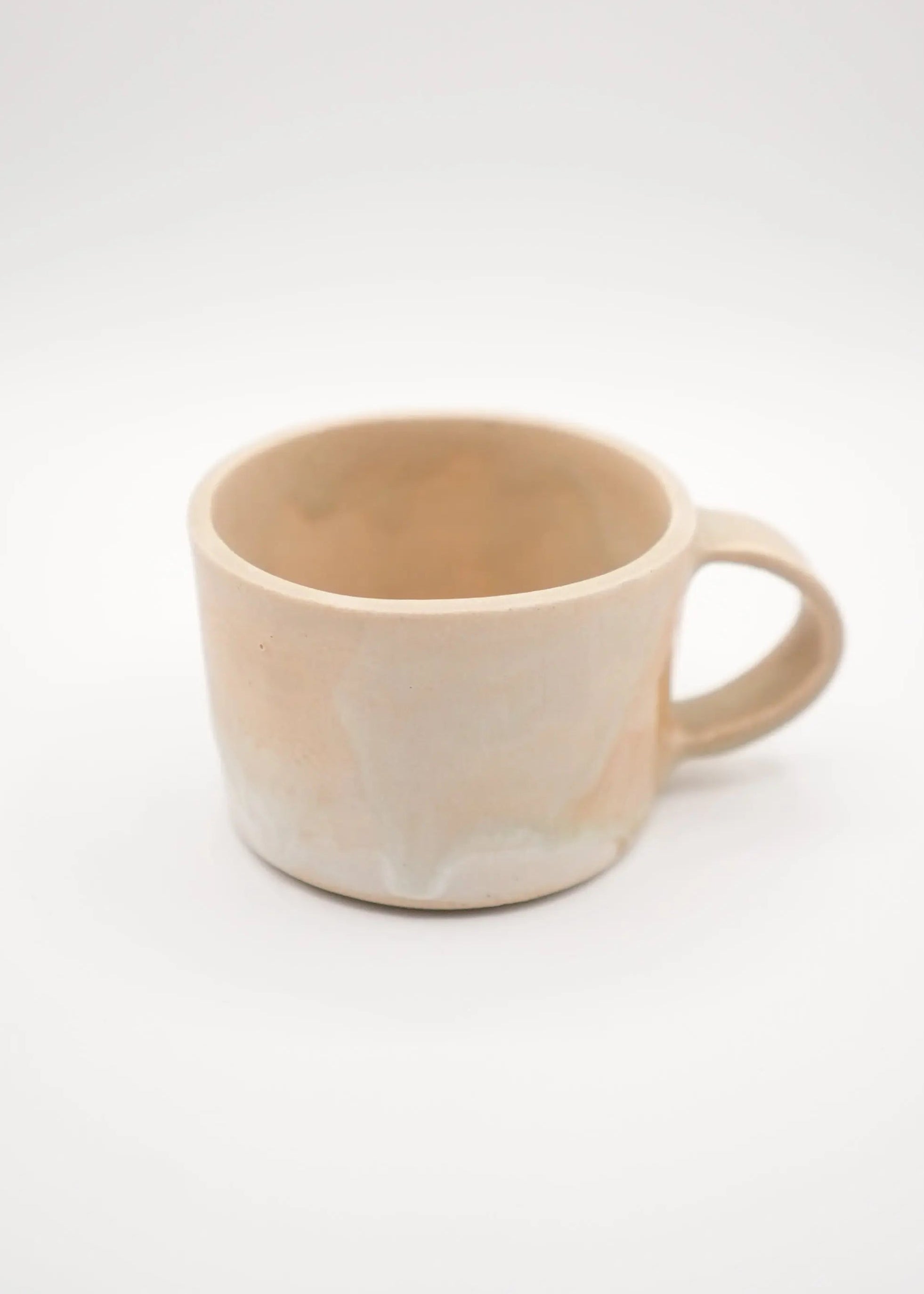 A handmade ceramic mug with a warm, earthy beige and light brown marbled glaze, shown against a seamless white studio background.