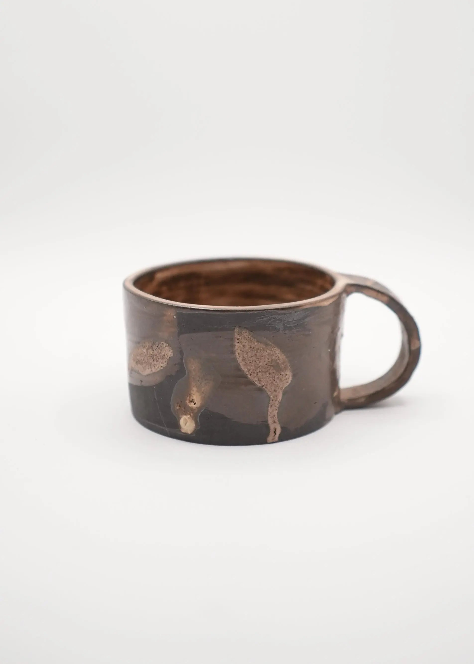 A dark brown ceramic mug with a handle, decorated with metallic gold leaf patterns, set against a plain light gray background.