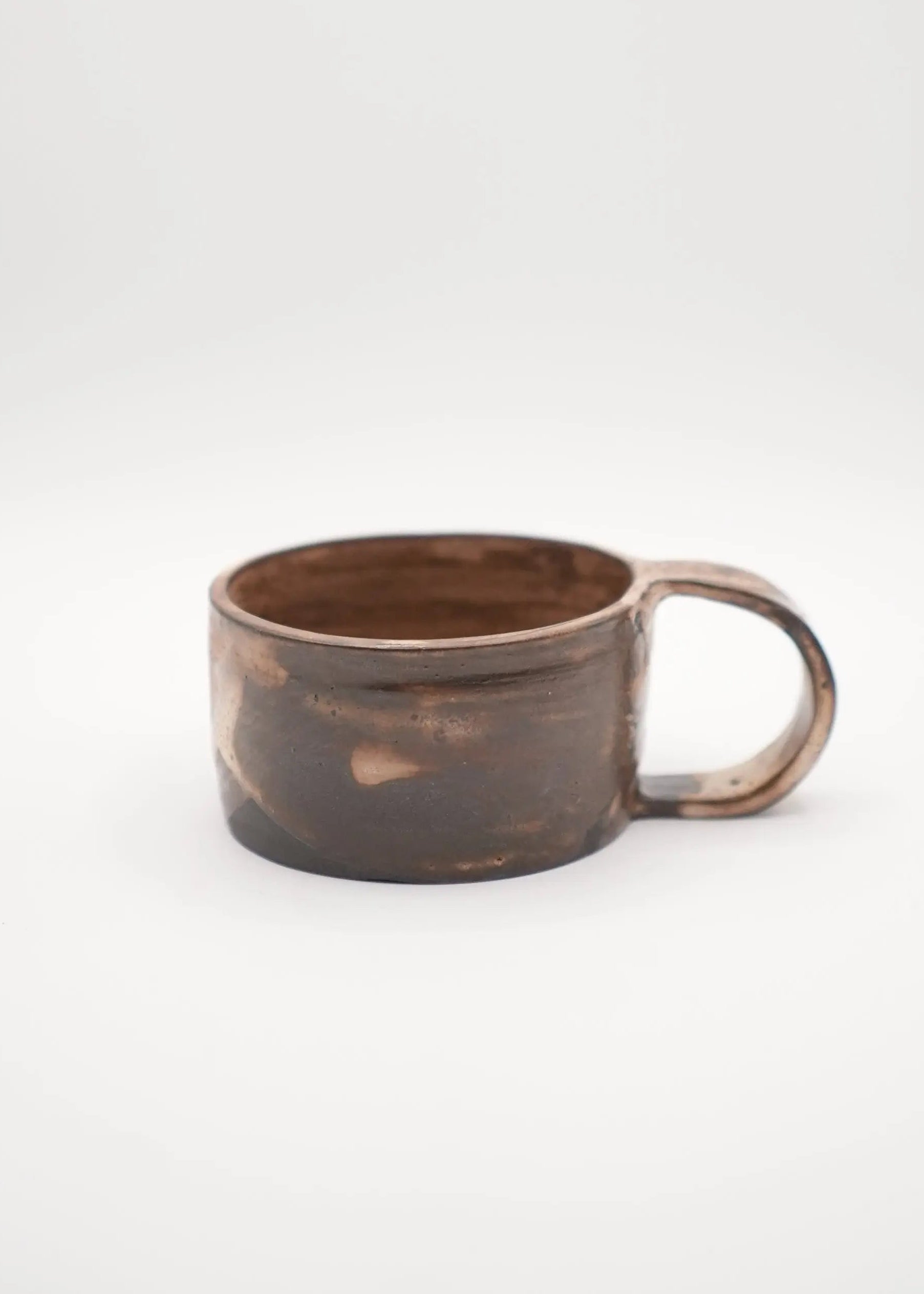 A rustic handmade ceramic mug with a dark brown and black textured glaze and a matching loop handle, set against a plain light gray background.