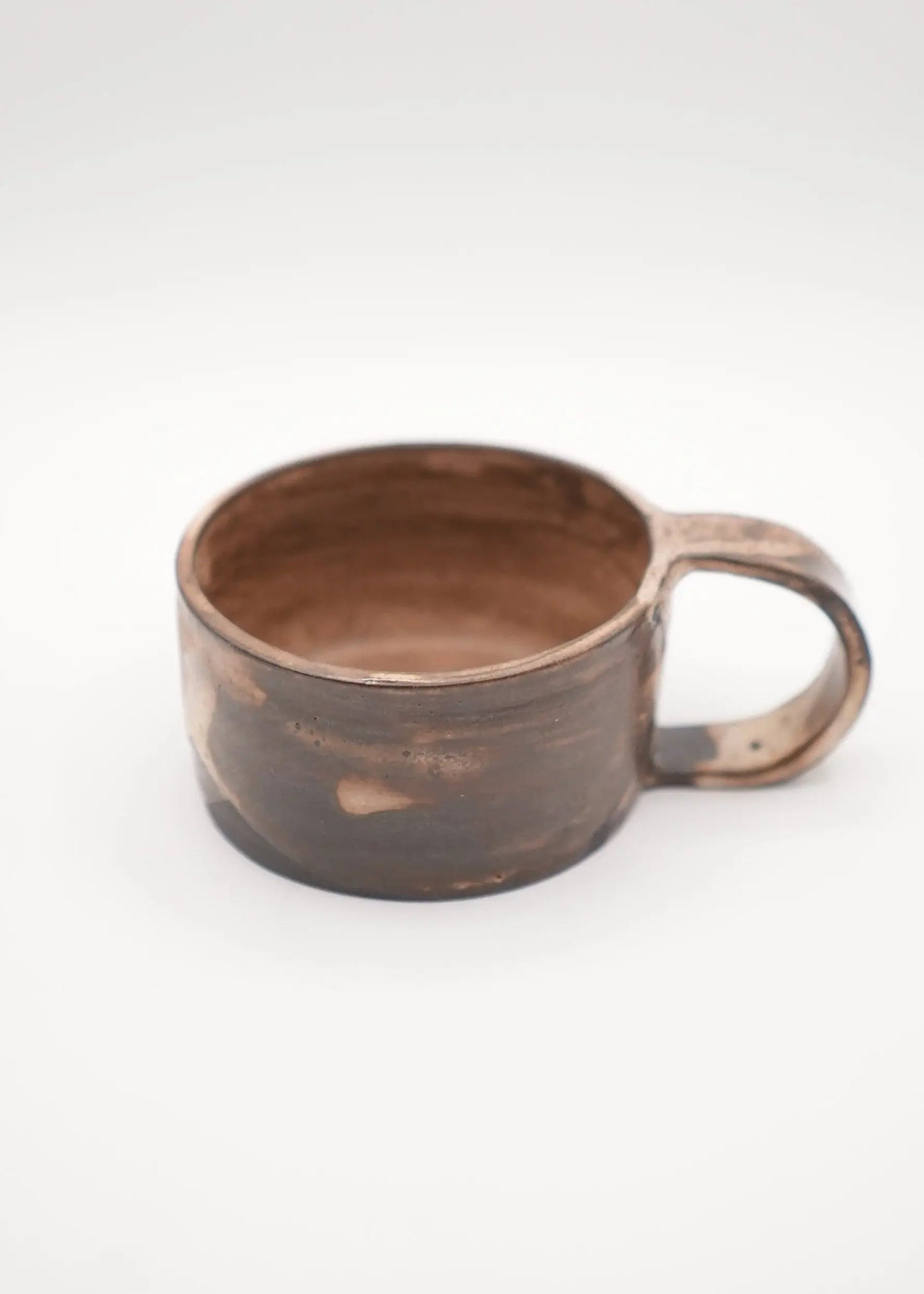 A rustic handmade ceramic mug with a dark brown and black textured glaze and a matching handle, shown on a light gray background.