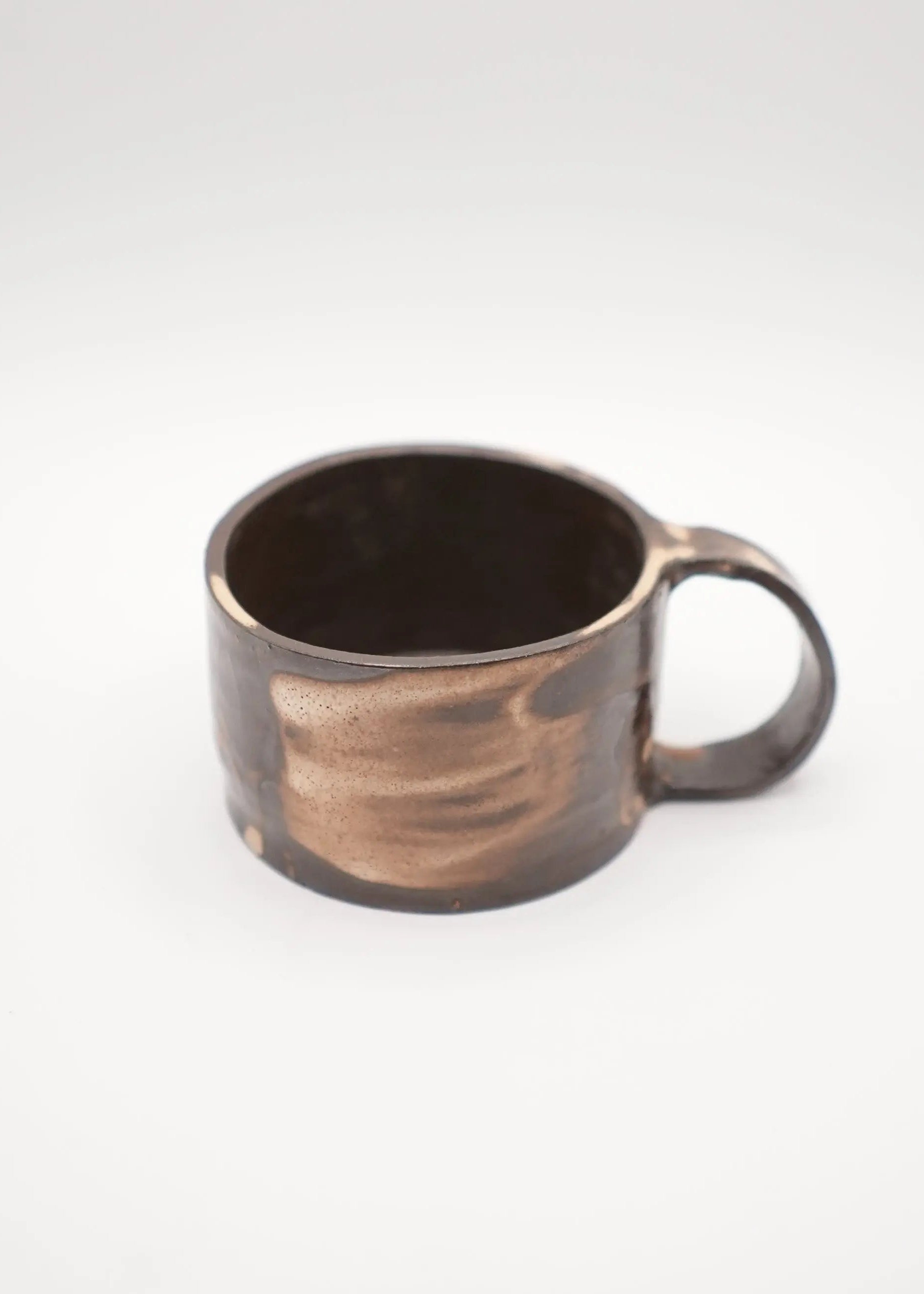 A handmade ceramic mug with a rustic, hand-painted finish in dark brown and bronze tones, set against a plain light gray background.